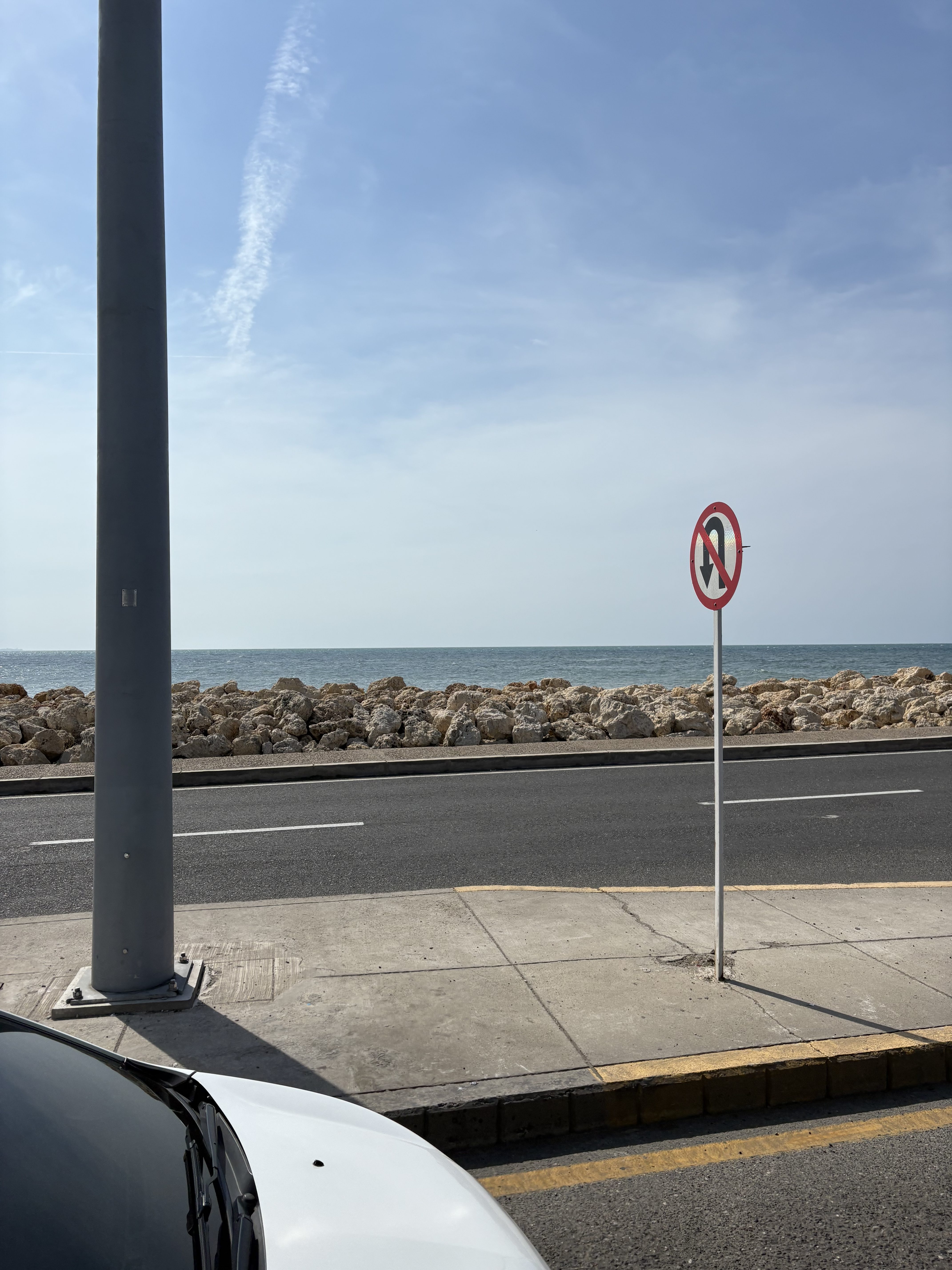 Coastal road with ocean view, cloudy sky, and a vehicle near the sidewalk.