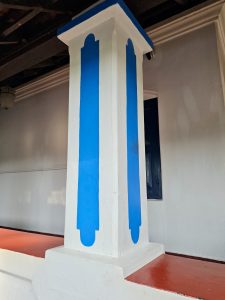 A blue and white pillar supports the veranda of a traditional Kerala house, showcasing simple design and clean architectural lines. Captured at Mangode, Puthunagaram, Palakkad.