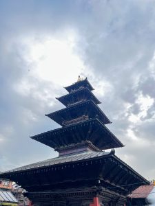 A low-angle shot of a traditional multi-roofed Newari pagoda temple against a cloudy sky.
