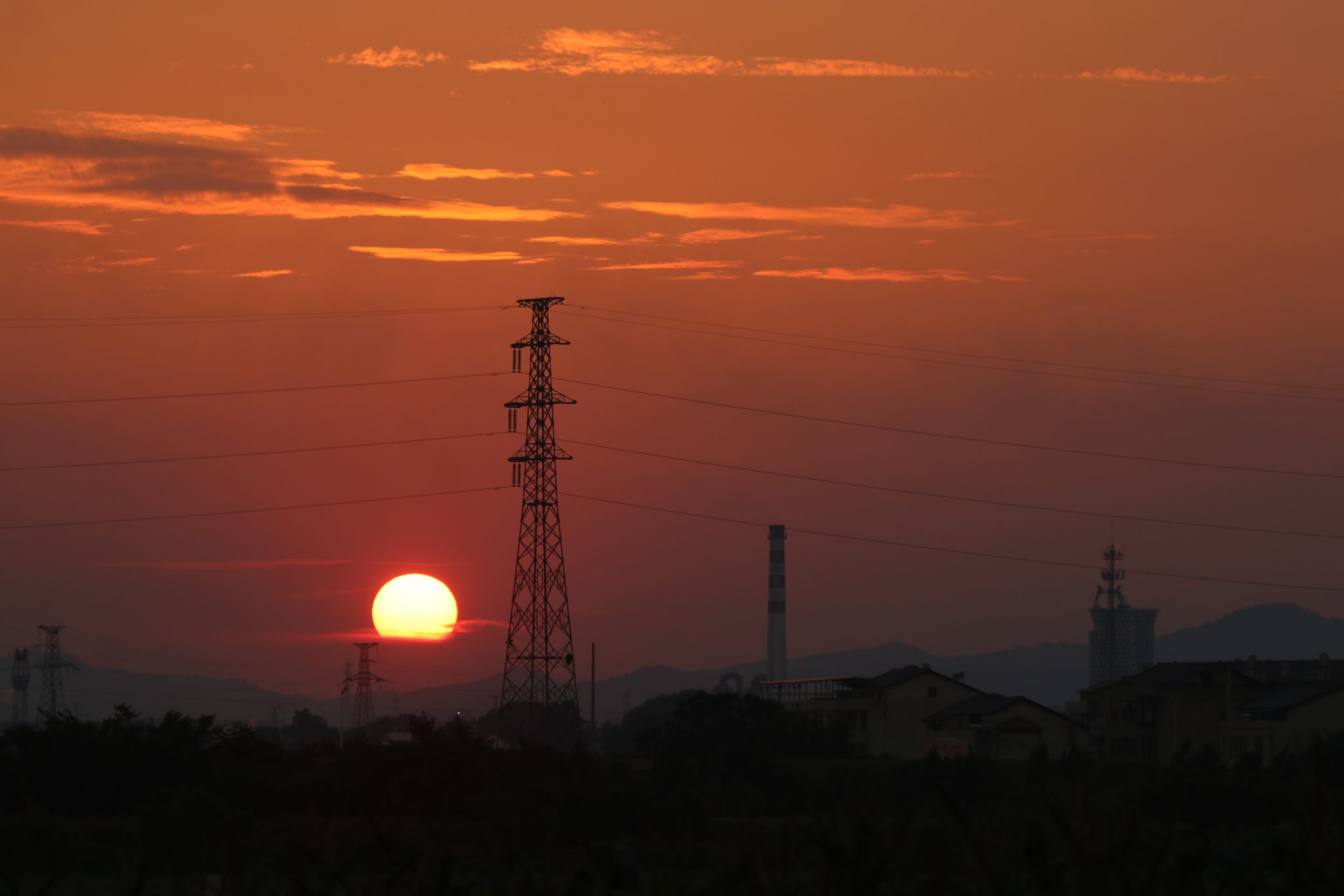 Torre de alta tensão recortada contra um céu ao pôr do sol, com linhas elétricas a atravessar a paisagem