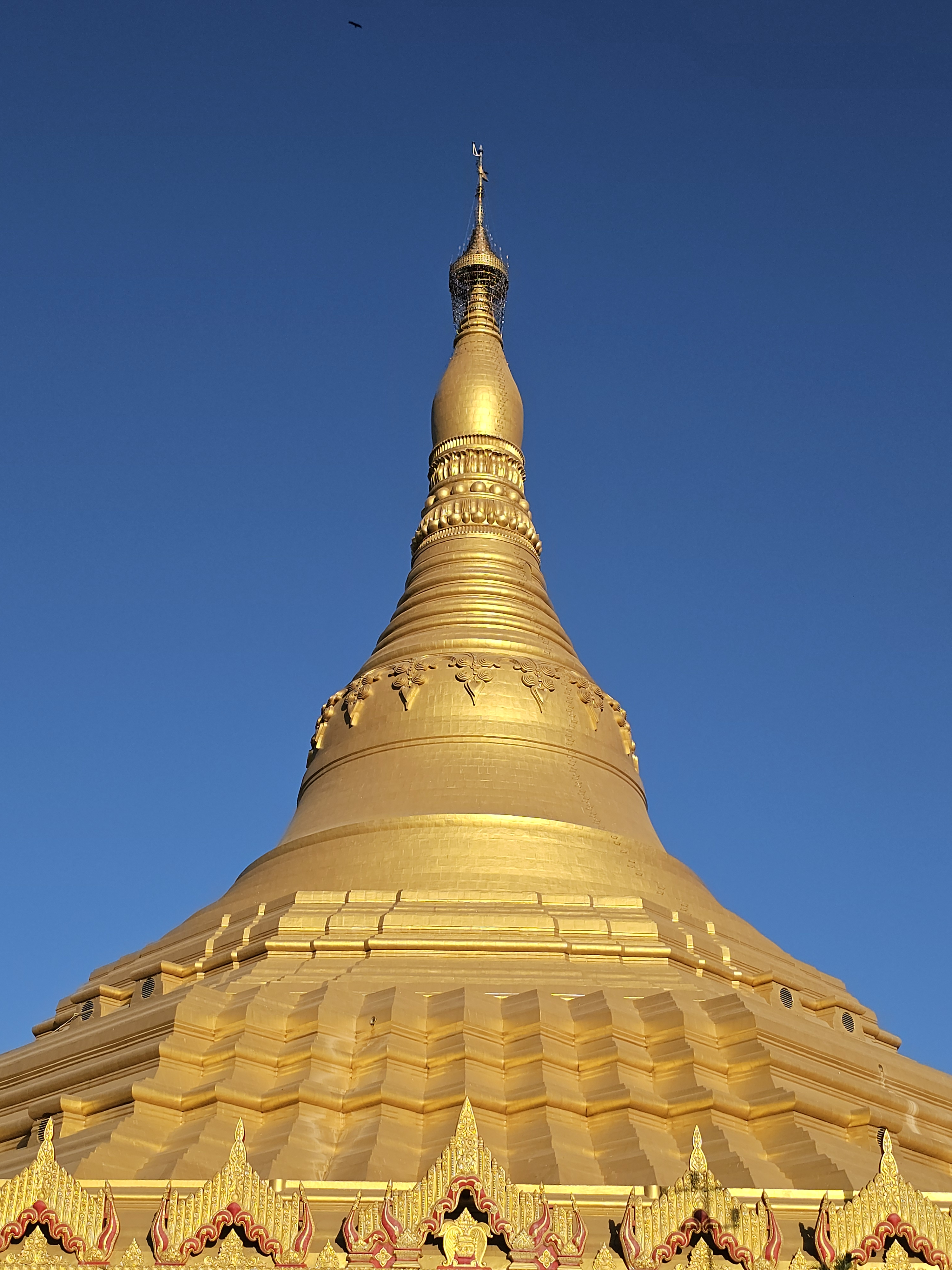 A low-angle view of the magnificent golden dome of the Global Vipassana Pagoda standing against a deep blue evening sky. The elegant architecture and warm light highlight the beauty of this peaceful Buddhist monument. Captured at Global Vipassana Pagoda, Gorai Village, Mumbai.