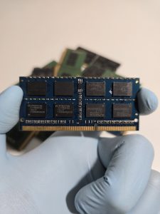 A close-up image of a hand in blue glove holding a SODIMM RAM module of DDR3 architecture.