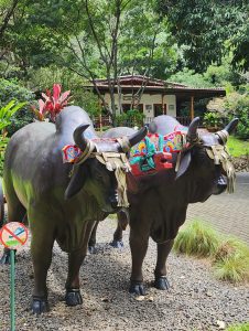 Two decorated cattle statues in a lush garden.
