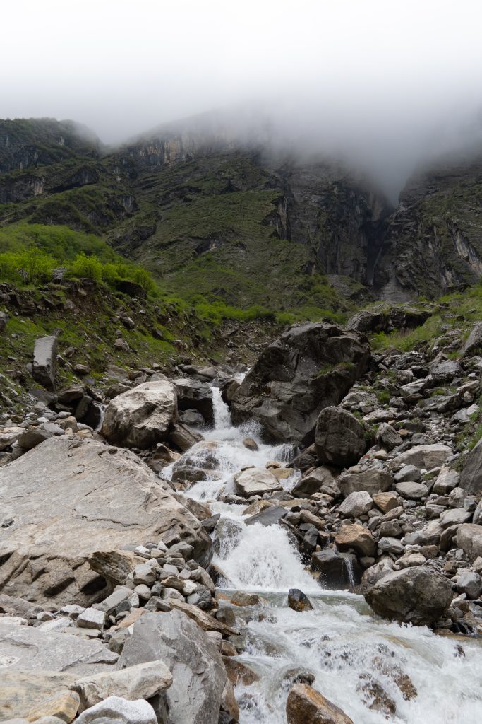 Rocky mountain stream cascading over boulders in a steep gorge with fog obscuring the upper cliffs