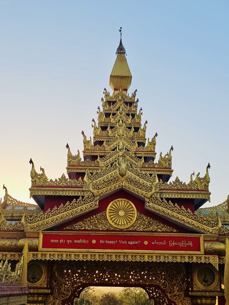 The beautifully decorated entrance gate welcomes visitors with intricate carvings, golden details, and traditional Buddhist architecture. The message "Be happy! Visit again!!" adds a warm touch to this peaceful place. Captured at Global Vipassana Pagoda, Gorai Village, Mumbai.