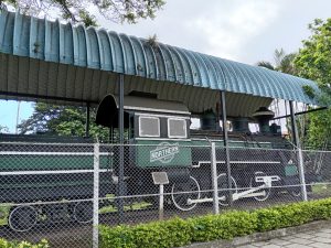 Preserved antique steam locomotive displayed under a metal roof in a park in Costa Rica.