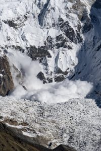 Avalanche cloud billowing down a steep rocky snow-covered mountain face of Nepal