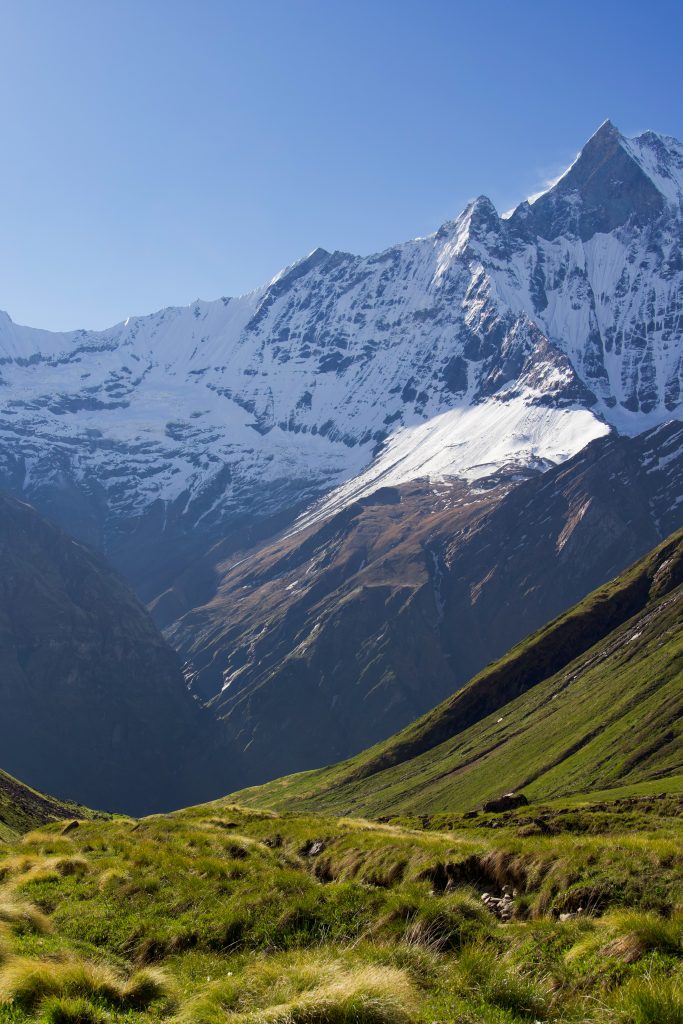 Sharp snow-covered mountain peak rising above green grassy slopes and a deep valley