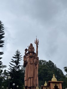 Large Lord Shiva statue surrounded by green trees.