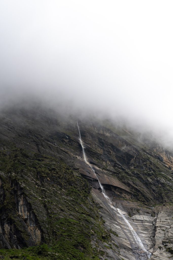 Thin waterfall streaming down a steep rocky mountain slope, upper section obscured by fog