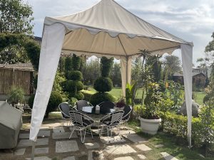 A serene outdoor patio with a white canopy covers a glass table surrounded by six black chairs. 