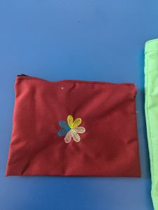 A maroon pencil bag with a colorful embroidered flower on a blue surface.
