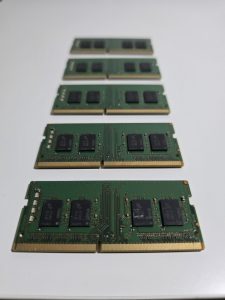 The image shows a series of SODIMM RAM, arranged in a slight diagonal line from the bottom left to the top right. Each module features a dark green circuit board with several small black chips embedded on it, arranged in pairs.