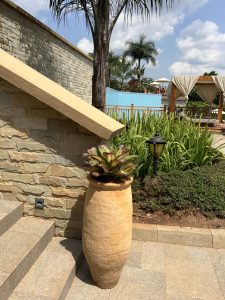 A tall ceramic planter containing a bromeliad stands beside a stone staircase and retaining wall. 
