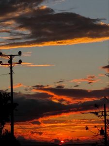 Sunset sky with glowing orange clouds and silhouetted utility poles.
