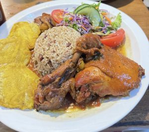 A plate with a seasoned chicken leg, rice with red beans, and two fried plantain slices.