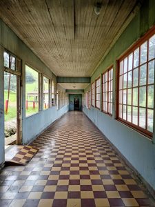 Long covered corridor at the Sanatorio Durán in Costa Rica, with a checkered tile floor and rows of windows overlooking the surrounding grounds.
