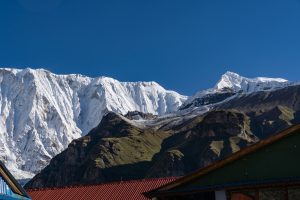 Snow-covered mountain ridge behind a green hillside with a red metal rooftop in the foreground