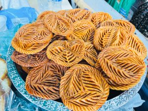 A large platter filled with intricately patterned, golden-brown fried sweets shaped like leaves, displayed at a market stall.