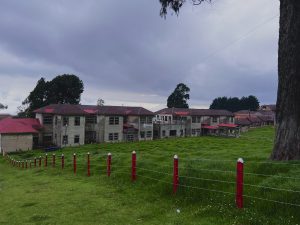 Large building with red roofs surrounded by green fields and cloudy skies.