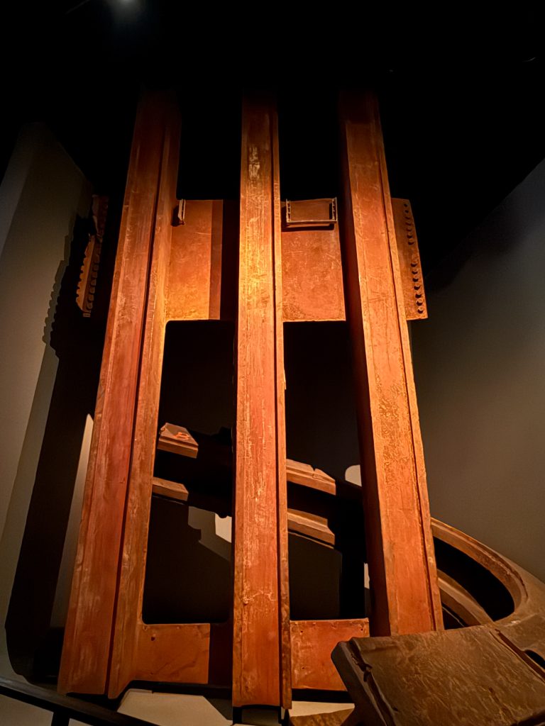 Part of the infrastructure of the former twin towers, now in the 9-11 museum and memorial. It is a large section of I-beams, orange in color, lit up in contrast of the dark room.