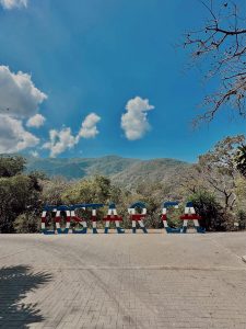 Colorful 'Costa Rica' sign in a woodland setting beneath a bright blue sky and clouds.