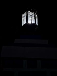 A traditional lantern glows against the dark night sky, creating a simple and peaceful scene. The light highlights the classic design of the old fixture. Captured at Mangode, Puthunagaram, Palakkad.