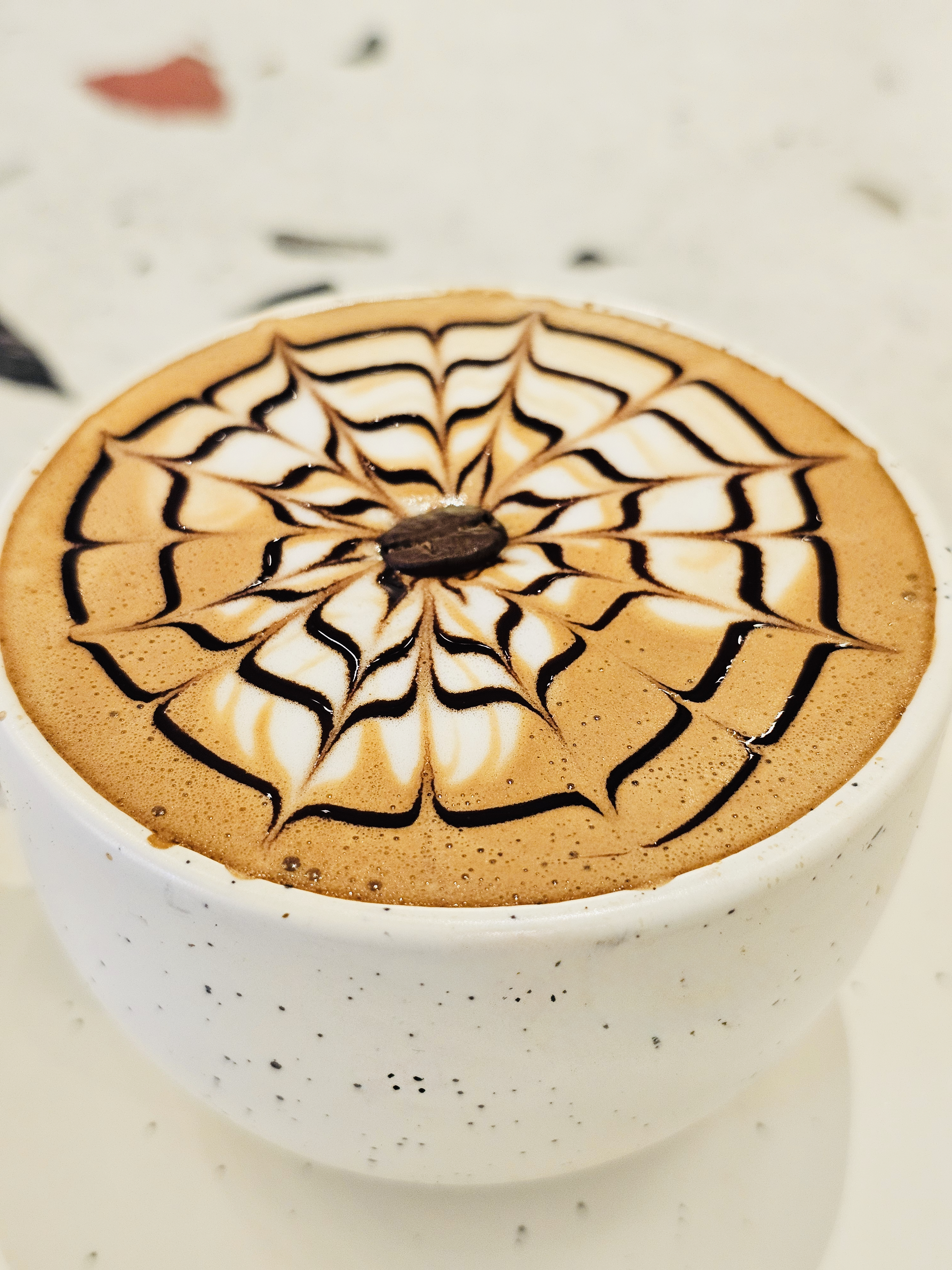 Creamy coffee is adorned with neat spiderweb latte art, making the drink both inviting and artistic. Captured in Pune, Maharashtra.