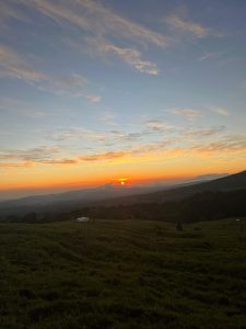 A picturesque sunset scene unfolds over rolling green hills. 
