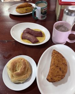 Plates with sausage on a tortilla, a fried pastry, and a cup of hot coffee.