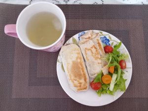 
Plate with two toasted wraps, salad, and a cup of lemon juice.