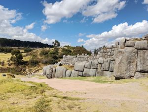 Road beside the stone walls of Sacsayhuaman, with the Cristo Blanco statue on a hill in the distance.