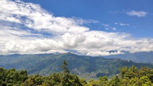 Scenic view of mountains from a hillside, showcasing lush greenery and a clear blue sky.