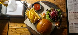 Gourmet burger with crispy French fries, fresh garden salad, and ketchup, beautifully served on a rustic wooden platter in a cozy restaurant
