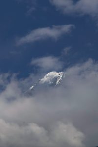 Snow-covered mountain peak partially surrounded by clouds against a blue sky