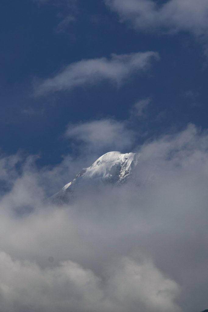Snow-covered mountain peak partially surrounded by clouds against a blue sky