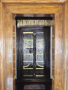 A traditional wooden doorway with brass fittings stands inside a historic Kerala home. Its polished wood and simple design reflect the beauty of heritage architecture. Captured at Mangode, Puthunagaram, Palakkad.