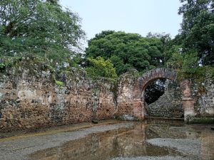 Historic stone archway in the Ujarrás church ruins with a rain-soaked courtyard.

