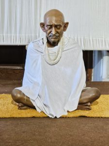 A peaceful statue of Mahatma Gandhi sits in a meditative pose, dressed in his simple white shawl, reflecting his values of truth, simplicity, and non-violence. Captured inside Aga Khan Palace, Pune, Maharashtra.
