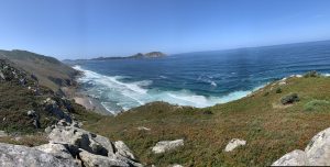 Panoramic view of the Costa da Vela cliffs in Cangas, with Melide Beach, a lighthouse, and the Cíes Islands on a clear day.