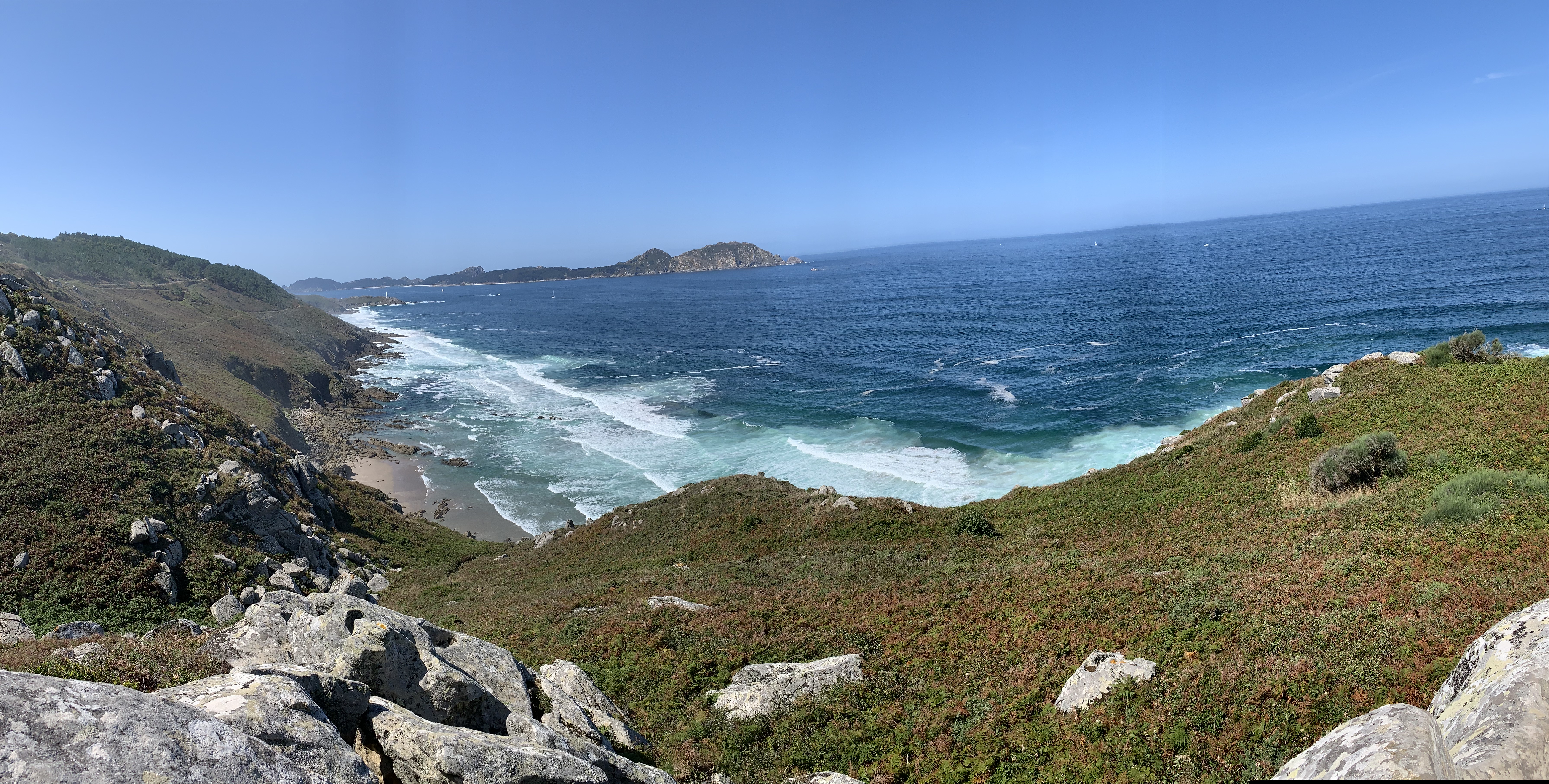 Panoramic view of the Costa da Vela cliffs in Cangas, with Melide Beach, a lighthouse, and the Cíes Islands on a clear day.