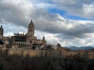 Panoramic view of Segovia Cathedral rising above the historic city walls in Segovia, Spain, beneath dramatic clouds.
