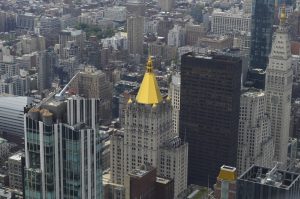 Elevated view of closely packed buildings of varying heights and architectural styles.  A historic building with a gold-colored pyramid-shaped roof stands out among the surrounding skyscrapers