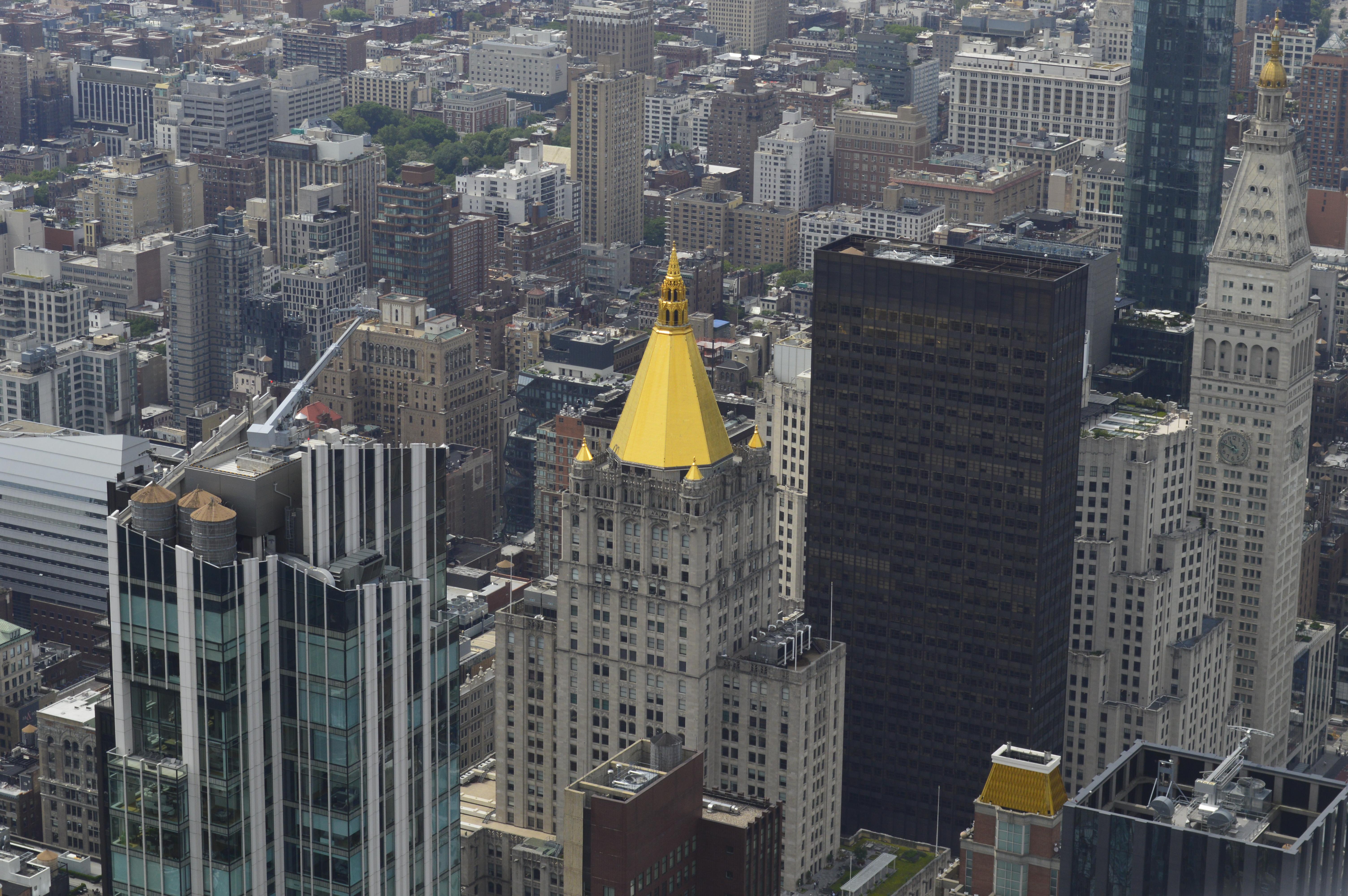 Elevated view of closely packed buildings of varying heights and architectural styles. A historic building with a gold-colored pyramid-shaped roof stands out among the surrounding skyscrapers