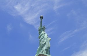 Low-angle view of the Statue of Liberty against a bright blue sky with thin, wispy clouds. 