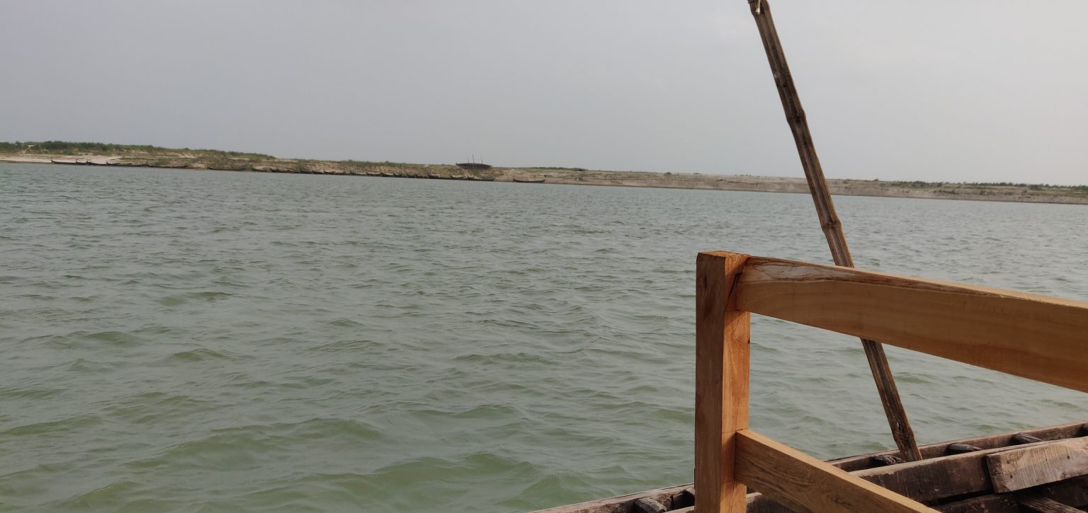 View of a calm river from a wooden boat under an overcast sky.