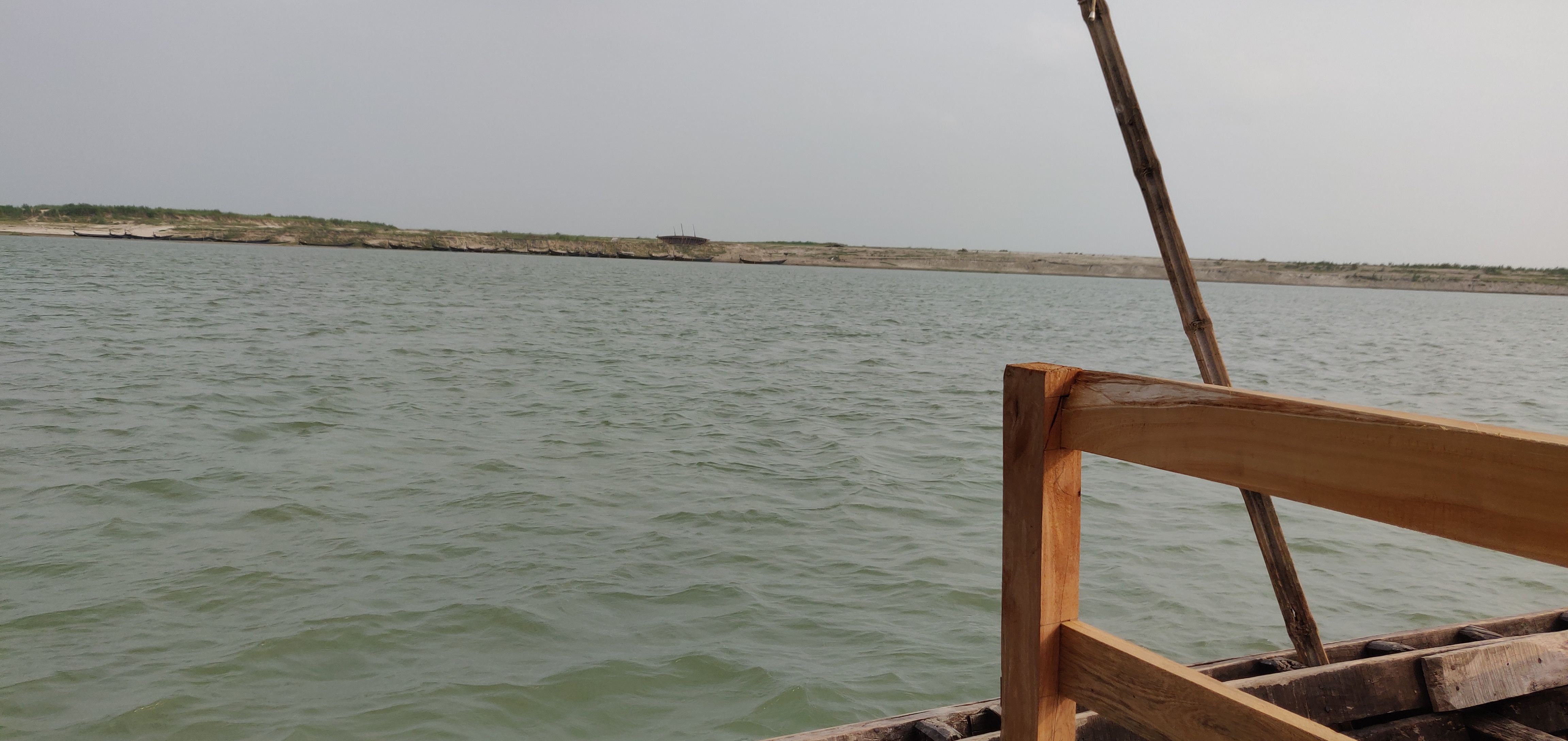 View of a calm river from a wooden boat under an overcast sky.