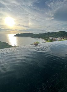 
A serene view from a luxurious infinity pool overlooking a calm beach and rolling hills. 