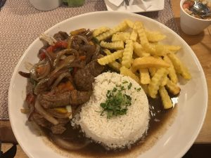 A large round plate contains a serving of rice shaped into a dome and topped with a sprinkle of fresh green herbs. Next to the rice is a portion of sautéed beef strips mixed with colorful vegetables, including bell peppers and onions, all coated in a savory brown sauce. 