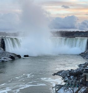 A winter view of Niagara Falls, surrounded by snow-covered ground and icy formations, showcasing the beauty of the season.
